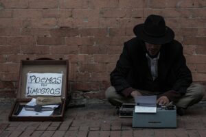 A writer in a black hat types poems on a typewriter, seeking donations on the street.