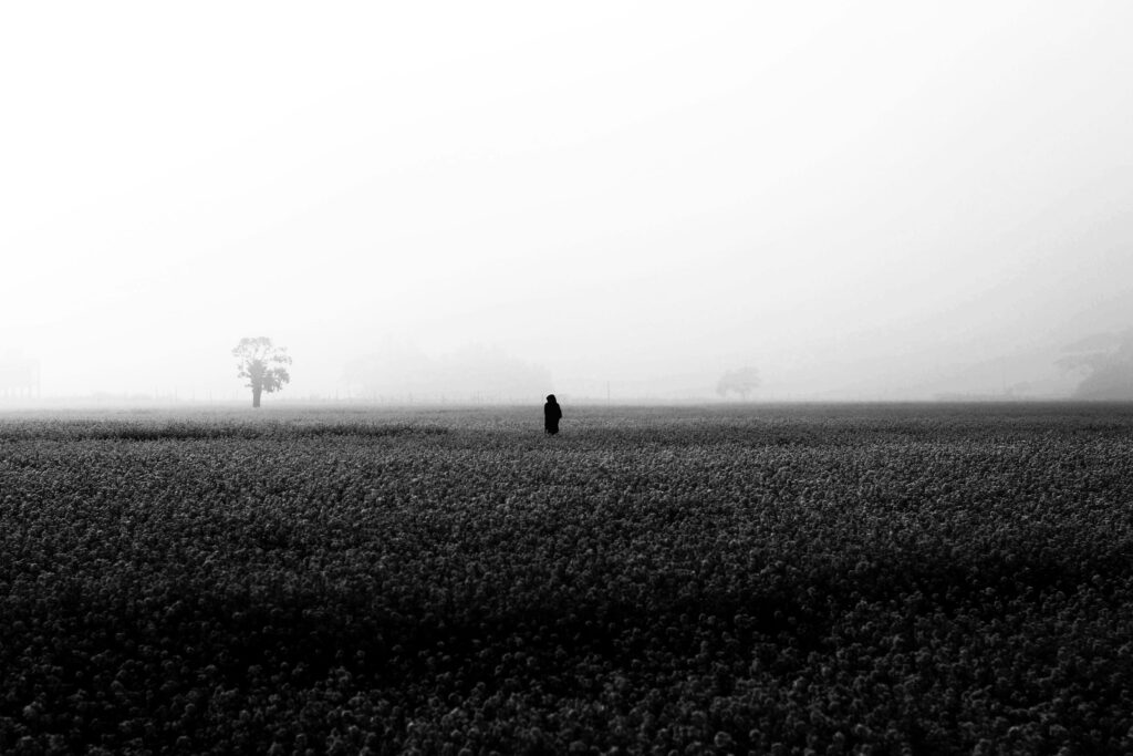 A solitary figure walks through a misty field in Bangladesh. Captivating black and white photography.