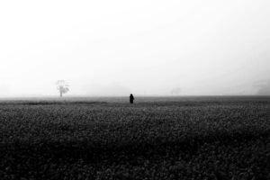 A solitary figure walks through a misty field in Bangladesh. Captivating black and white photography.